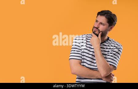 Nachdenklicher Mann, der aufblickt und auf Gelb nach Gelegenheiten sucht. Neugieriger bärtiger Kerl, der eine Lösung plant. Stockfoto