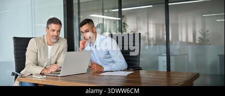 Zwei geschäftige Geschäftsleute arbeiten im Büro mit einem Laptop zusammen. Stockfoto
