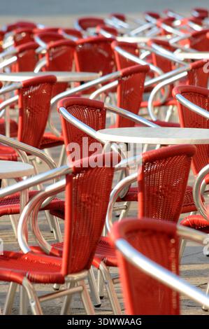 Reihen roter Café-Stühle und Tische im Sitzbereich im Freien, die sich wiederholende Muster auf der Terrasse des Restaurants schaffen. Stockfoto