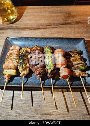 Verschiedene Yakitori, Fleischspieße auf schwarzer Keramikplatte mit gegrilltem Rindfleisch, Hühnchen und Gemüse im Restaurant, japanische Küche, Restaurant di Stockfoto