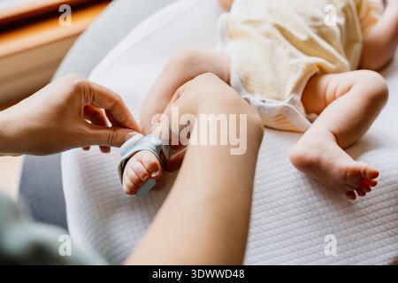 Eltern sichern tragbare Gesundheitsmonitor Socke am Fuß des Säuglings, während das Baby zu Hause auf Wickelauflage liegt, SIDS-Prävention, Überwachung von Säuglingen Stockfoto