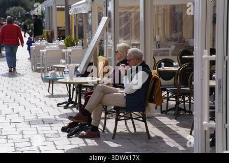 Älteres Ehepaar, das sich auf der Außenterrasse des Cafés an der sonnigen Promenade der französischen Riviera entspannt. Menton, Frankreich Stockfoto