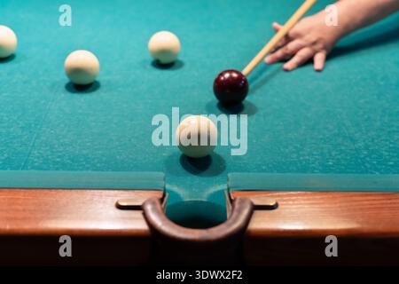 Männliche Hand, die Einen Cue-Stick auf den Roten Ball auf Einem grünen Billardtisch zielt. Stockfoto