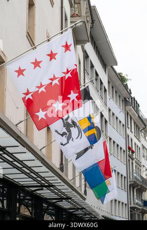 Eine Reihe von Schweizer Kantonsflaggen, darunter Wallis, Graubünden, Basel-Stadt, Tessin, Waadt und Zürich, ausgestellt in einem modernen Gebäude im Zentrum von Luzern. Stockfoto
