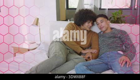 Kuscheln zwei Männer, die sich im hellen Schlafzimmer auf das Bett lehnen, mit Pullover, Nachttischlampe sichtbar Stockfoto