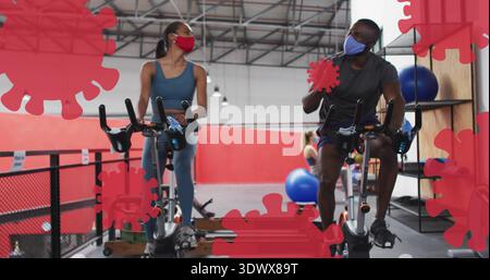 Fahrradduo mit Masken, Sportausrüstung im Fitnessstudio auf Heimfahrrädern, rote Virusüberzüge, blauer Ball Stockfoto