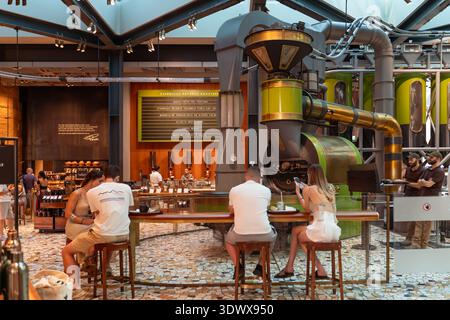 Szene der Kaffeekultur: Gäste sitzen an einer Holztheke mit Blick auf industrielle Röstergeräte in Mailands Starbucks Reserve Roastery. Stockfoto