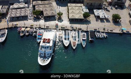 Luftaufnahme des Yachthafens von Sivota, Griechenland. Drohnenaufnahme von Ausflugs- und Fischerbooten, die am Pier mit kristallklarem türkisfarbenem Meerwasser angereiht sind. Stockfoto
