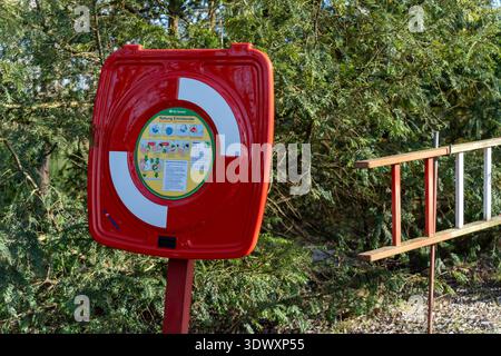 Eine detaillierte Ansicht zeigt eine rote Rettungsbox mit Anweisungen. Die helle Farbe steht im Kontrast zum umgebenden Grün. Stockfoto