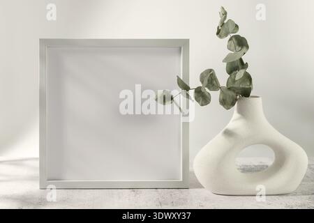 Leerer heller hölzerner Bilderrahmen und getrocknete natürliche Eukalyptuszweige in moderner Donut-Form Keramikvase auf Grunge-Steintisch vor neutraler Wand Stockfoto