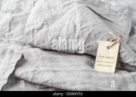 Gefaltete Serviette aus natürlichem hellgrauem Leinen mit Seil und Papieranhänger mit Text Stoffservietten 100% Pure Leinen. Stoffhintergrund im Vintage-Stil mit Cop Stockfoto