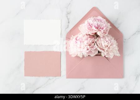 Leere Papierkarten und offener rosafarbener Retro-Umschlag mit Pfingstrosenblüten auf weißem Marmorhintergrund. Einladungskarte mit Blumenmuster im Vintage-Stil. Mockup-Geburtstag Stockfoto