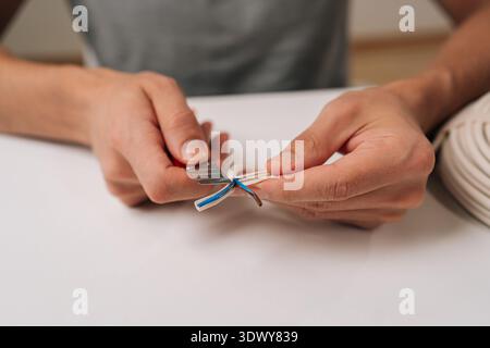 Elektrische Hände aus nächster Nähe, die moderne Datenkabel mit einem Schneidmesser aufteilen und innere Drähte freigeben, die für die Netzwerkeinrichtung und das Internet unverzichtbar sind Stockfoto