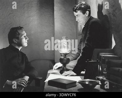 Ein dramatischer Schwarz-weiß-Film aus „The Keys of the Kingdom“ (1944) mit Vincent Price und Gregory Peck in klerikalen Gewändern. Price, der an einem Schreibtisch sitzt, blickt in einem intensiven Gespräch zu Peck auf und unterstreicht den ernsten Ton des Films. Stockfoto