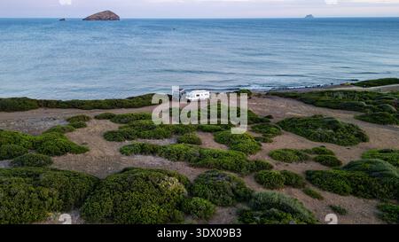 Ein atemberaubender Blick über die Drohne auf zwei Wohnmobile, die auf einer hohen Klippe mit Blick auf das Meer in Sardinien geparkt sind. Das Bild fängt das Wesen der Freiheit und ein Stockfoto