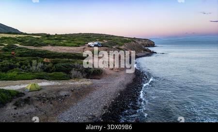 Der weite Panoramablick auf die Drohne fängt das Wesen des Vanlife und Abenteuers ein. Zwei Wohnmobile und ein kleines grünes Zelt befinden sich auf einer Klippe und einem Kieselstein Stockfoto