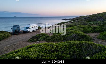 Ein atemberaubender Blick über die Drohne auf zwei Wohnmobile, die auf einer hohen Klippe mit Blick auf das Meer in Sardinien geparkt sind. Das Bild fängt das Wesen der Freiheit und ein Stockfoto