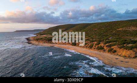 Panoramablick auf die Küste von Arbus während der goldenen Stunde. Die Aufnahme fängt den Kontrast zwischen den üppigen Hügeln ein, die mit mediterranem Gestrüpp bedeckt sind, Stockfoto