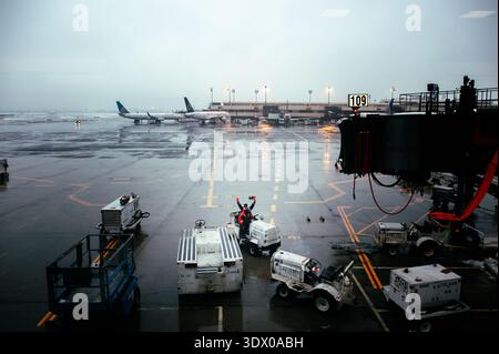 Ein Mitglied der Bodenbesatzung winkt von einem Schlepper auf einem regnerischen Asphalt des Newark Liberty International Airport mit United- und Star Alliance-Flugzeugen am Gate 109. Stockfoto