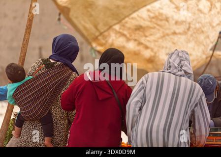 163 drei einheimische Frauen in Djellaba-Kleidung drängen sich um einen Verkaufsstand im zentralen Souk, wo sie Obst und Gemüse auf dem Dienstagsmarkt verkaufen. Rissani-Marokko. Stockfoto