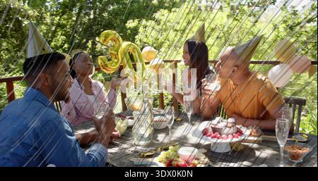 Wir feiern vier Freunde in Kegel-Partyhüten, die auf dem Hinterhof mit 30 goldenen Ballons toasten Stockfoto