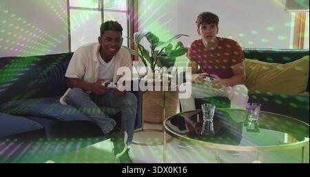 Freunde spielen, die weiße Controller auf dem marineblauen Sofa zu Hause in lässiger Kleidung mit grünem Licht halten Stockfoto
