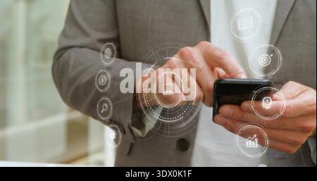 Schwarzer Smartphone-Mann in grauem Anzug mit weißen Handschellen im Büro mit digitalen Symbolen Stockfoto