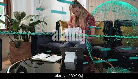 Schreiberfrau in rotem Oberteil und Jeans auf Sofa zu Hause mit Papieren, Tablet, blaugrünen Überzügen Stockfoto
