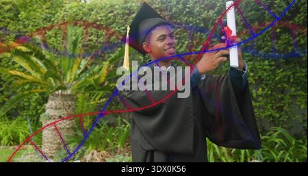 Lächelnder männlicher Absolvent in schwarzem Kleid und Mortarboard mit Diplom im Garten, Helix-Überzug Stockfoto