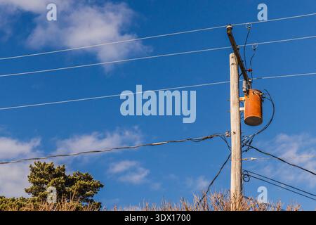 Elektrischer Transformator am hölzernen Versorgungsmast in den USA mit Stromleitungen und blauem Himmel Stockfoto