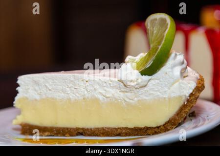 Eine Scheibe Limettenkuchen mit Schlagsahne und einem Limettenkeil liegt auf einem weißen Teller. Stockfoto