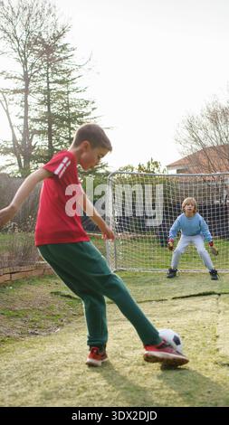 Jungen, die den Fußball in Richtung Tor treten, einer als Torhüter Stockfoto