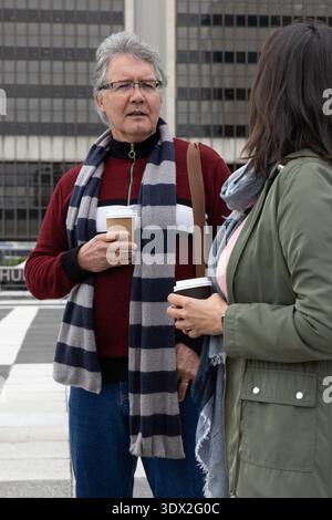 Seniorenmann und Erwachsene Frau plaudern vor dem plaza-Büro, halten To-go-Kaffee und tragen Schal Stockfoto