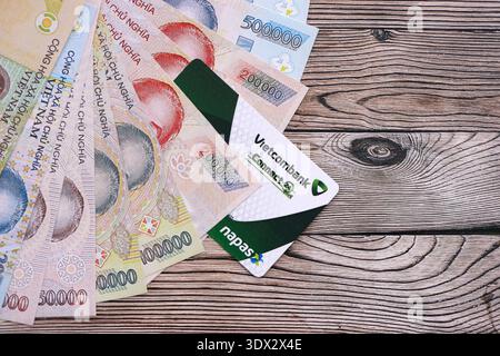 KIEW, UKRAINE - 28. JANUAR 2026 Vietcombank-Karte und vietnamesische Dong-Geldscheine auf dem Tisch in Nahaufnahme. Die Vietcombank ist die beliebteste Bank in Vietnam Stockfoto