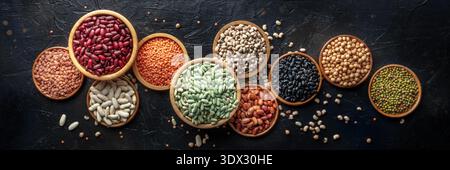 Verschiedene Leguminosen, oben flach liegendes Panorama auf schwarzem Hintergrund. Viele verschiedene Impulse, ein Sortiment, Panorama-Banner Stockfoto
