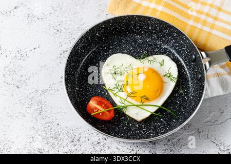 а herzförmiges Ei in einer Pfanne ohne Öl gebraten, mit grünen Zwiebeln und Dill gewürzt. Gesundes Frühstückskonzept. Schale mit Handtuch auf Steinlasche Stockfoto