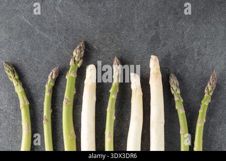 Grüner und weißer roher Spargel auf grauem Steintisch. Saisonales Frühlingsgemüse für gesunde Ernährung. Dunkler Hintergrund mit Kopierraum Stockfoto