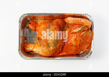 Mariniert in Tomatensauce mit Kräutern rohe Hälfte des Hühnchens in einer Einweg-Backverpackung aus Aluminium auf weißem Hintergrund. Verpackung von Produkten in Sup Stockfoto