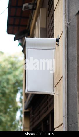 Weißes leeres Ladenschild, das an einer Wandfläche des Gebäudes hängt, für benutzerdefinierten Text und Logo Stockfoto
