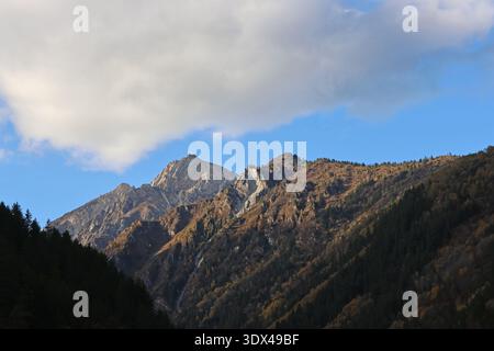 Nachmittagsblick auf schneebedeckte Berge, dramatische Wolken und farbenfrohe Wälder im Herbst im Jiuzhai Valley National Park in China Stockfoto