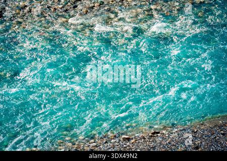 Gekräuseltes kristallklares, türkisfarbenes Flusswasser, das über glatte Steine und Kieselsteine in der Schlucht fließt Stockfoto