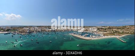Panoramablick auf die Marsaxlokk Bay mit Hafenmachtpunkt, verankerten Booten, Stadt am Wasser und türkisfarbenem Mittelmeer unter klarem Sommerhimmel. Stockfoto