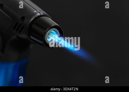 Ein leistungsstarker Gasanzünder. Feuerzeug mit blauer Flamme auf schwarzem Hintergrund. Stockfoto