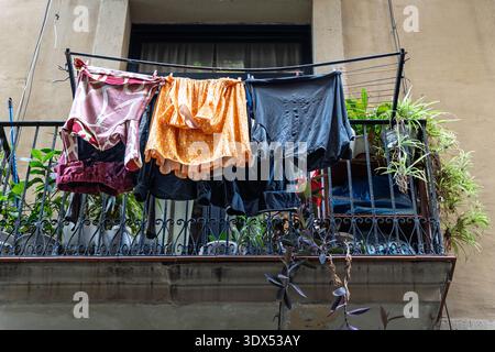 Bunte Kleidung hängt auf einem Wäscheständer über einem schmiedeeisernen Balkon mit grünen Pflanzen in einem Viertel von Barcelona. Stockfoto