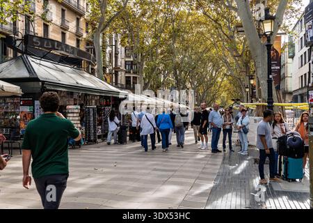 Barcelona, Spanien - 1. November 2025. Touristen und Einheimische spazieren die breite, von Bäumen gesäumte Promenade der La Rambla Straße unter sonnigem Himmel hinunter. Massentourismus, ur Stockfoto