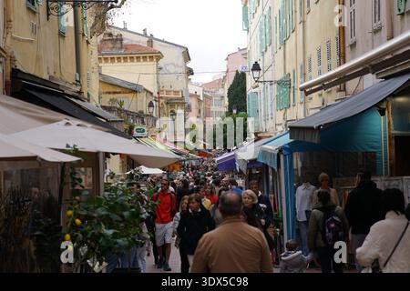 Belebte Fußgängerzone in Mentons farbenfroher Altstadt mit Touristen, Geschäften und Zitronenpflanzen unter einem lebhaften mediterranen Himmel. Menton, Frankreich Stockfoto