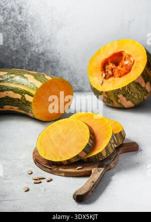 Frischer Kürbis ‚Madeira‘ (Cucurbita moschata), geschnitten auf einem Holzschneidebrett mit Messer und Samen. Rustikales Stillleben des tropischen Kürbis Stockfoto
