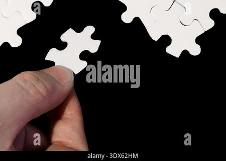 Nahaufnahme der Hand, die das weiße Puzzleteil auf schwarzem Hintergrund platziert Stockfoto