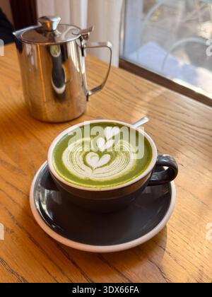 Matcha Latte und Metall-Teekanne auf Holztisch. Warmes Licht, ausgewogene und langsame Café-Atmosphäre. Stockfoto