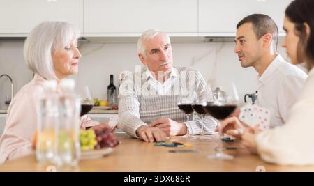 Fröhliche Senioreneltern und ein junges Paar sitzen am Tisch und spielen Poker Stockfoto